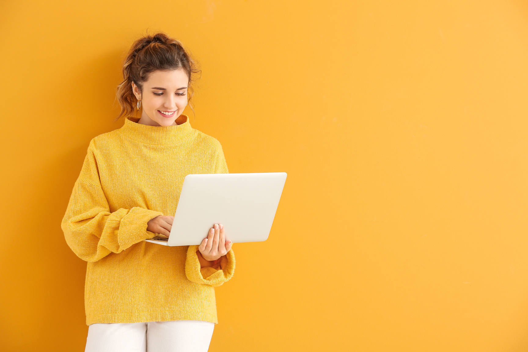 Beautiful Young Woman in Warm Sweater and with Laptop on Color Background